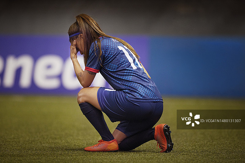 沮丧的女足球运动员跪着，双手抱头表示失望图片素材