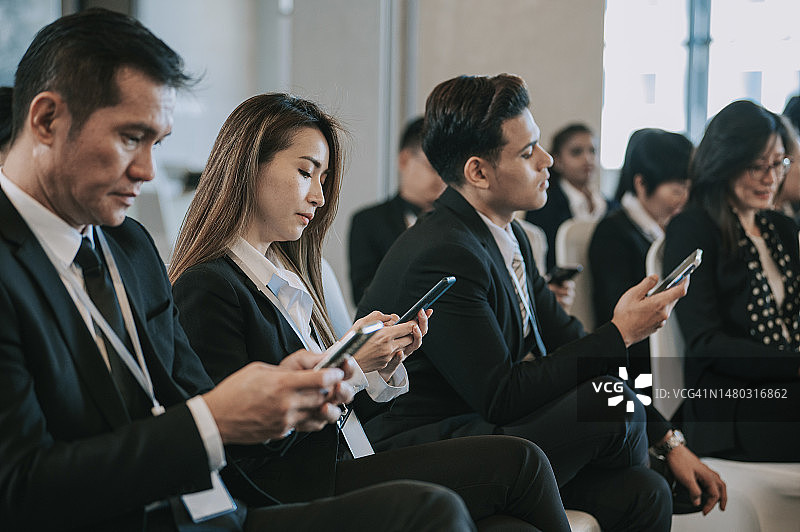 中国研讨会参与者在商务会议室等待时使用智能手机发短信图片素材