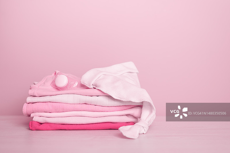 粉色背景上的新生婴儿干净衣物堆叠特写，留有文字空间，婴儿期和母性概念图片素材
