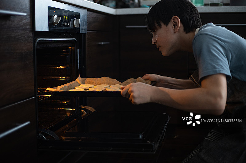 青少年将装有饼干的烤盘放入烤箱图片素材