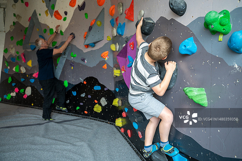 儿童与祖父在室内人造攀岩墙上攀岩图片素材