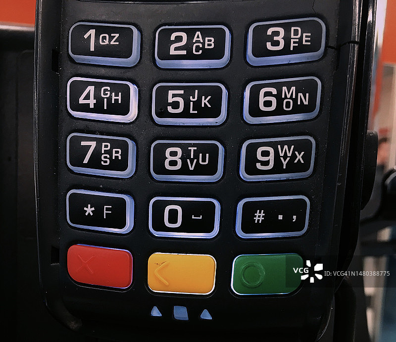 带有红色和黄橙色按钮的支付终端特写图片素材