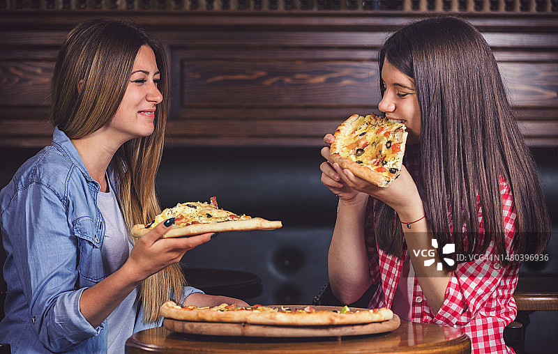 两名少女在餐厅享用美味披萨图片素材