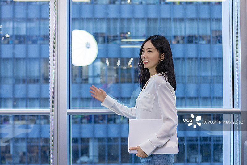 一位年轻女士手持笔记本电脑站在窗前的肖像图片素材