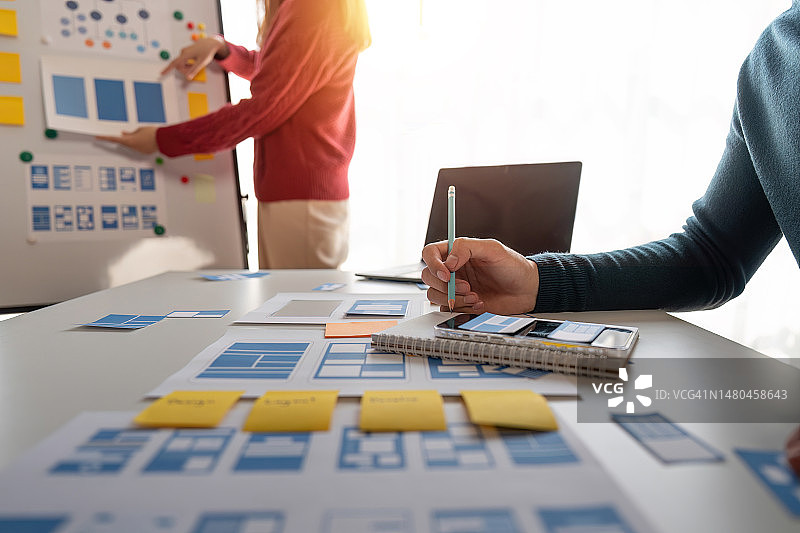 UI设计师和UX开发者在现代办公室讨论手机App界面线框图设计特写图片素材