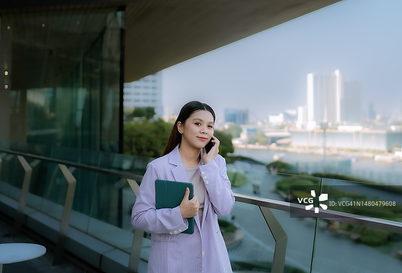 在豪华大厦露台上等待的亚洲年轻女性给客户打电话图片素材
