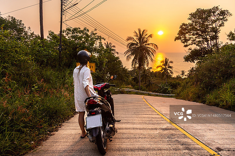 女游客在泰国岛屿上骑着摩托车欣赏日落美景图片素材