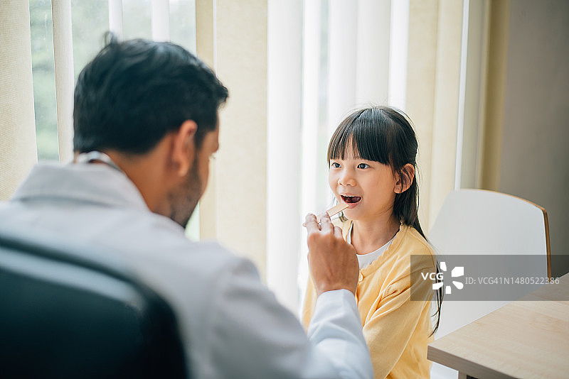 亚裔印度医生在他的办公室检查女孩的喉咙。图片素材