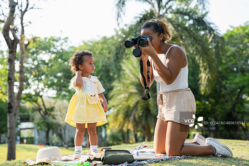 年轻母亲和女儿在阳光明媚的日子里在公园里玩双筒望远镜图片素材