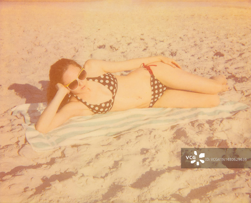 在沙滩上穿着波点比基尼晒日光浴的复古女郎图片素材