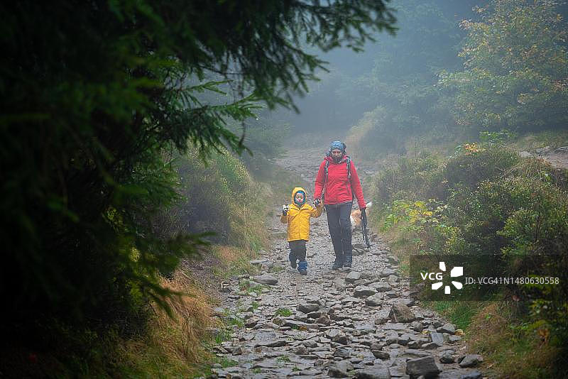 妈妈和小儿子在潮湿的秋天里走在山路上，还有一条狗陪伴，波兰山区图片素材