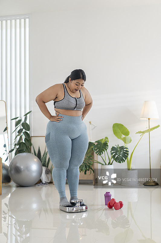 成功的减肥：坐在体重秤上的超重年轻女人图片素材