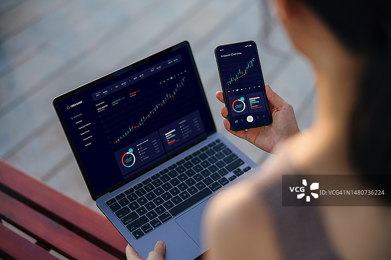 亚洲女商人在线管理财务和投资，分析股票市场交易，并使用笔记本电脑和智能手机制定财务计划的肩部视角。网上银行。银行、金融、投资和金融交易概念图片素材