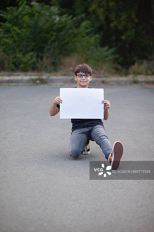一个蹲在一只腿上，拿着白色标志的白人男孩（12-13岁）图片素材