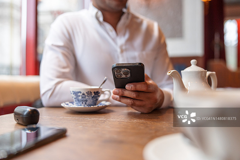 深色皮肤的男人在咖啡馆桌子上拿着iPhone手机的手图片素材
