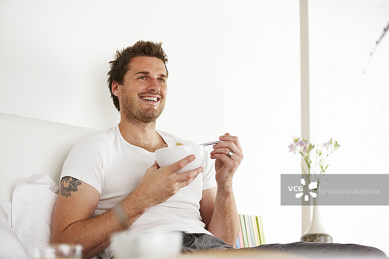 年轻男人卧室吃早餐图片素材