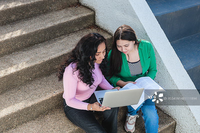 两个拉丁女学生在楼梯校园里用笔记本电脑和书本学习图片素材