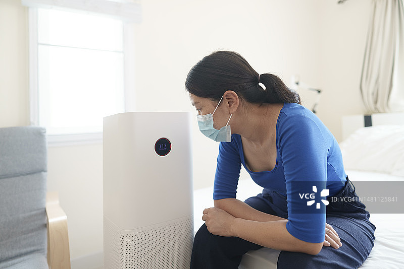 负面情绪和不健康的环境：空气污染PM2.5，亚洲成年女性戴N95口罩，在泰国清迈卧室拥抱空气净化器过滤器深呼吸图片素材