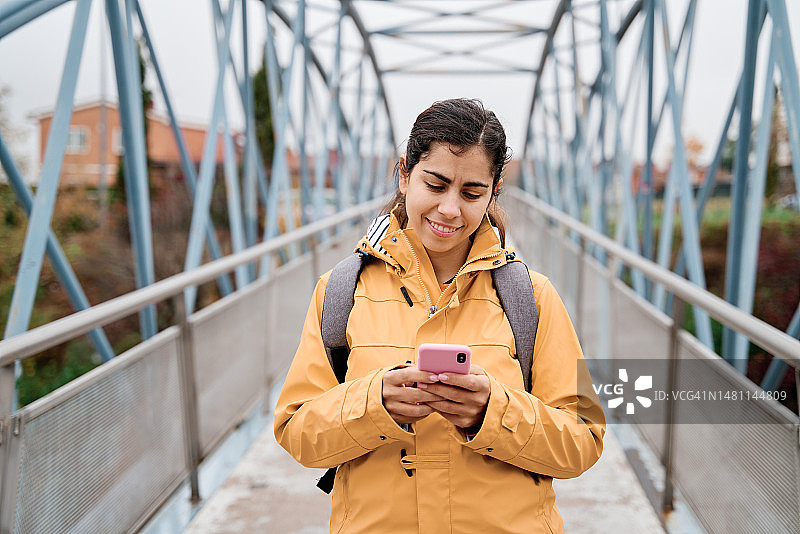 微笑的女人在桥上使用智能手机图片素材