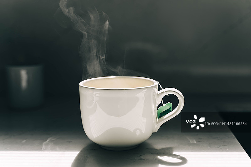 深色背景上的白色马克杯热茶，带茶包和蒸汽图片素材