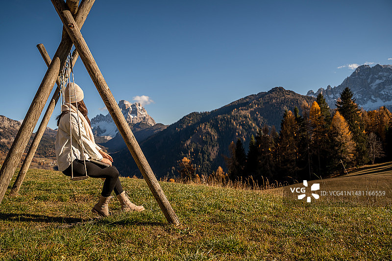 戴着针织帽和夹克的女人在日落时看着山脉图片素材