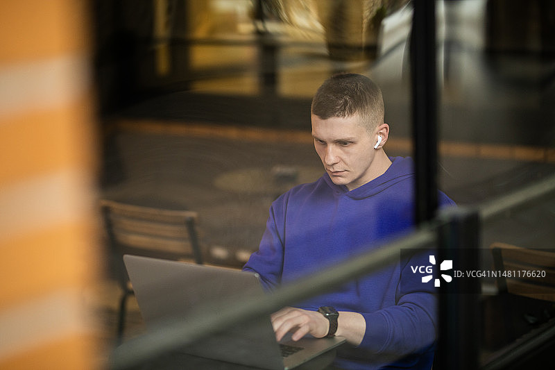 戴着无线耳机和笔记本电脑，专注工作的年轻男人图片素材