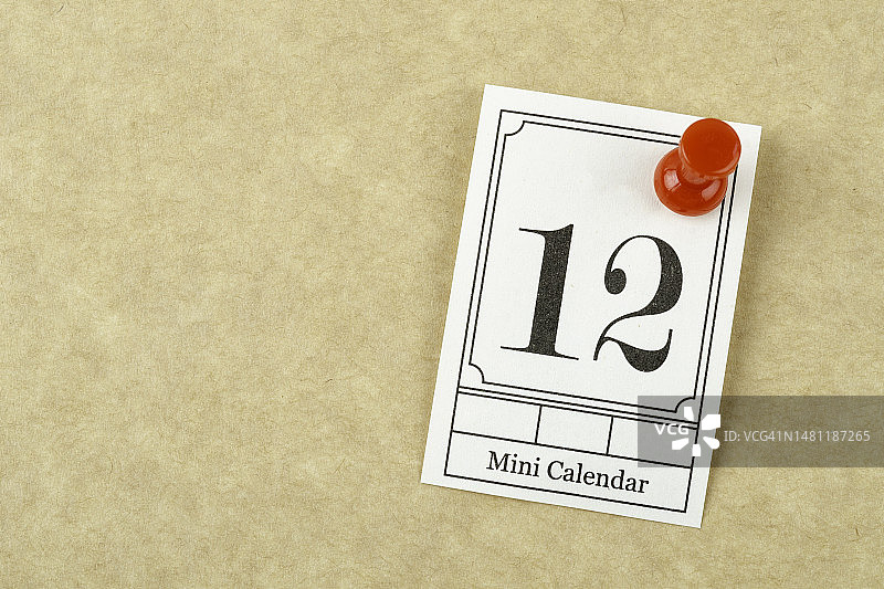 浅黄色背景上钉着12号日期的迷你日历图片素材