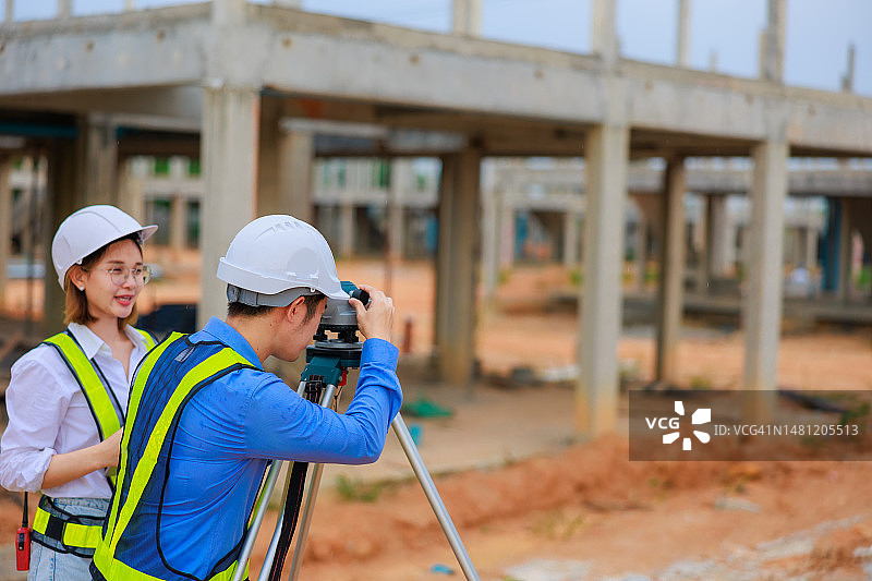 在建筑工地指导戴安全帽和反光背心的测量学徒的亚裔男工程师图片素材