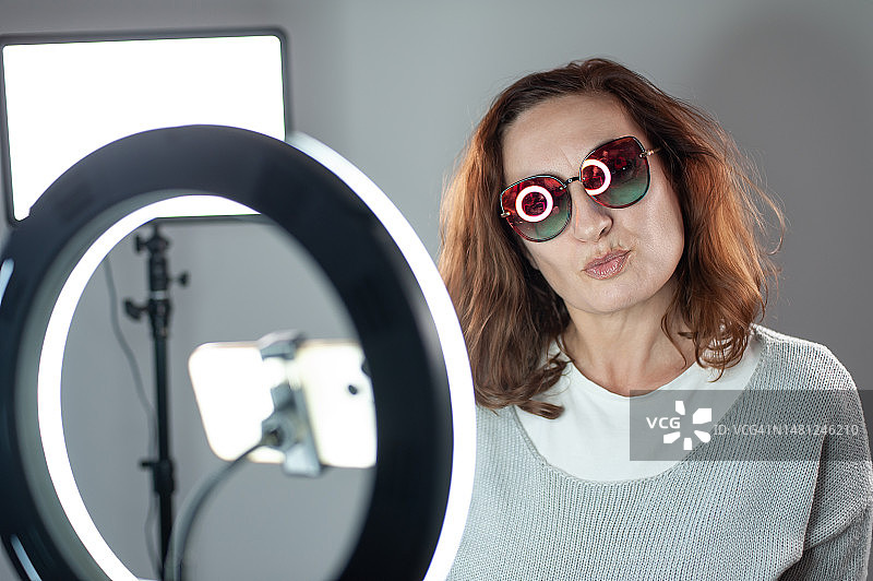 快乐的女网红坐在环形灯旁使用智能手机图片素材