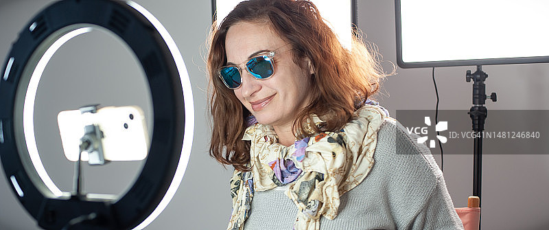 快乐的女网红坐在环形灯旁使用智能手机图片素材