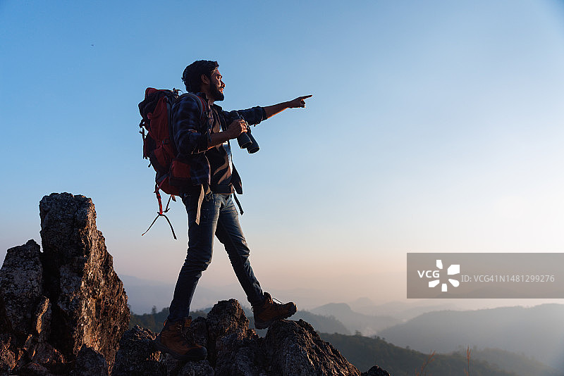 站在山顶指向天空的亚洲背包客图片素材