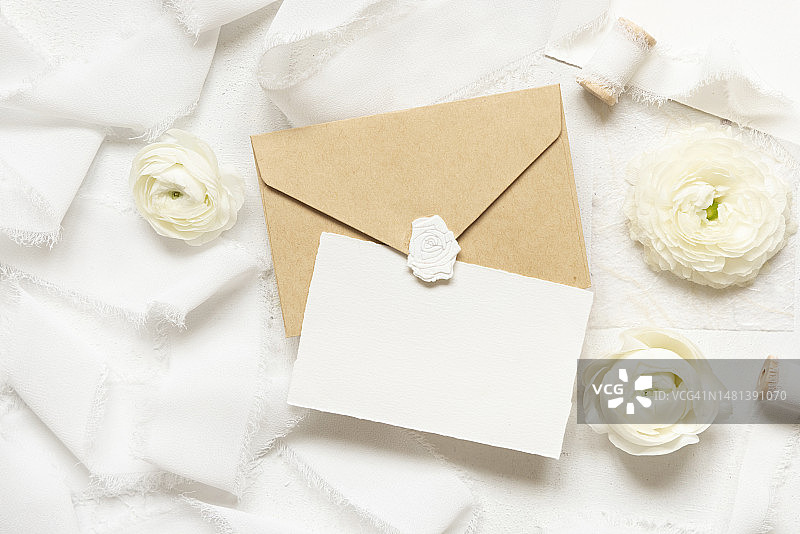 奶油色玫瑰和白色丝带附近的空白卡片和信封顶部视图，婚礼模型，意大利布林迪西图片素材