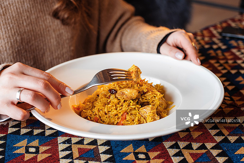 一位身份不明的女士在餐厅的餐桌旁吃肉抓饭图片素材