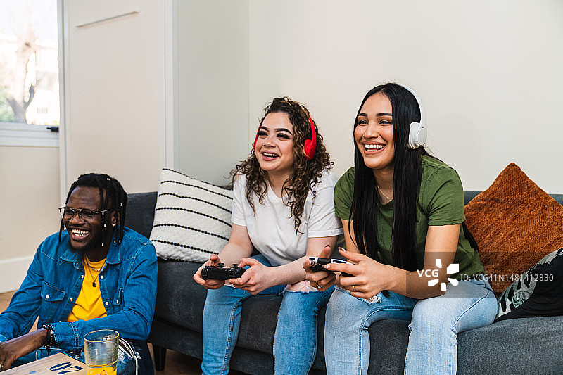 多元文化游戏乐趣：三个微笑的年轻人在客厅里戴着耳机玩游戏机图片素材