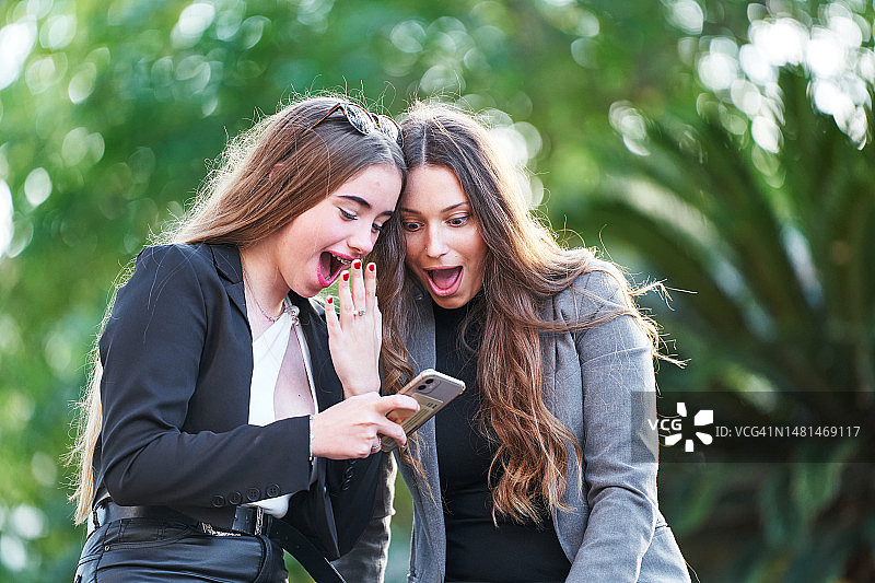 户外看手机的惊讶女人们图片素材