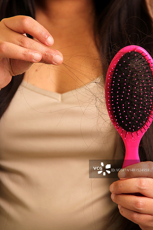 因疾病脱发，看着刷子上掉落头发的拉丁裔成年女子图片素材