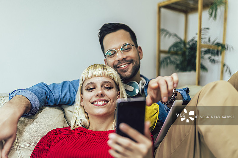 情侣在沙发上放松拥抱，使用平板电脑和手机图片素材