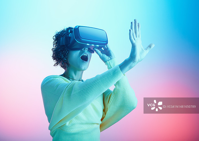 年轻女人戴着VR眼镜体验在多色背景下的虚拟现实图片素材