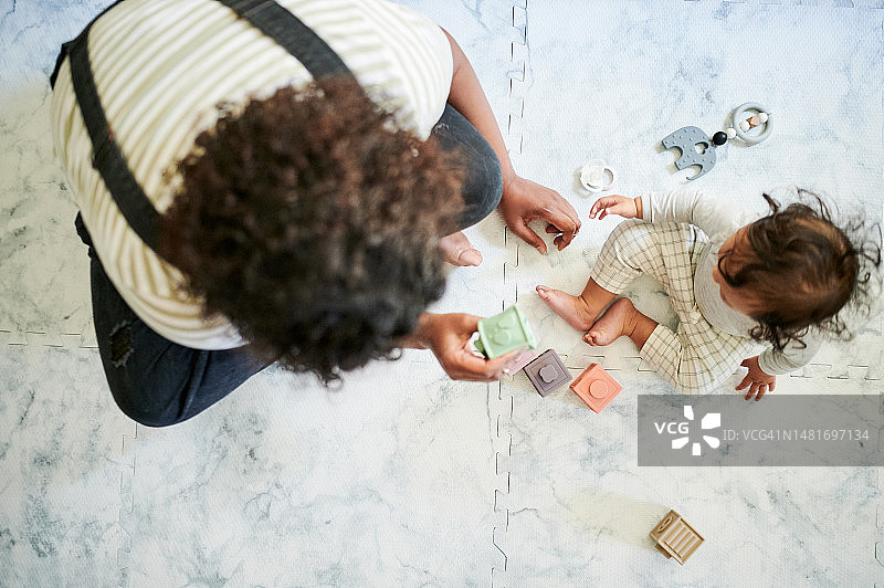 在家里，母亲和婴儿在地板上玩积木，用于教育、亲子互动和玩耍。学习，玩具和父母与幼儿玩魔方游戏的儿童发展俯视图图片素材
