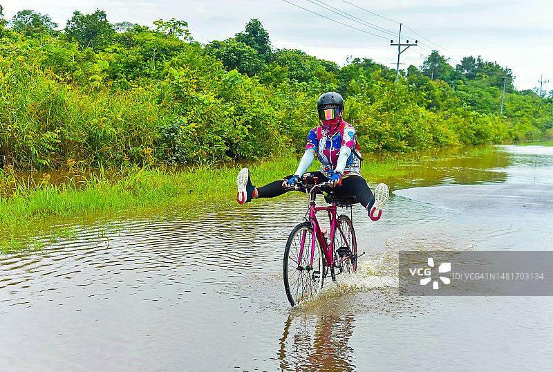 中年亚洲女人在被洪水淹没的道路上骑自行车图片素材