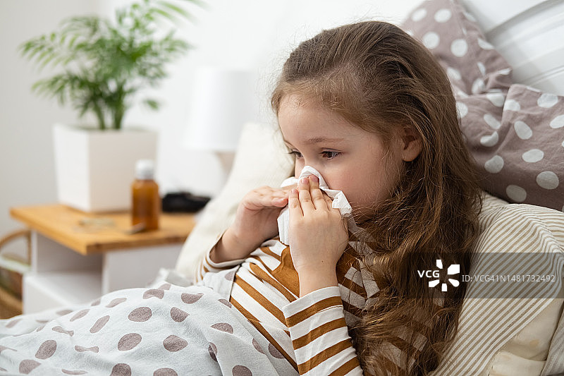 患流感的小白人女孩坐在床上擤鼻涕生病的孩子流鼻涕图片素材