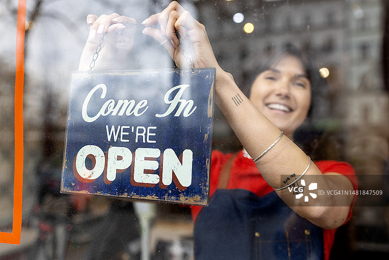 在零浪费食品店工作的女人将开业标志挂在玻璃门上图片素材