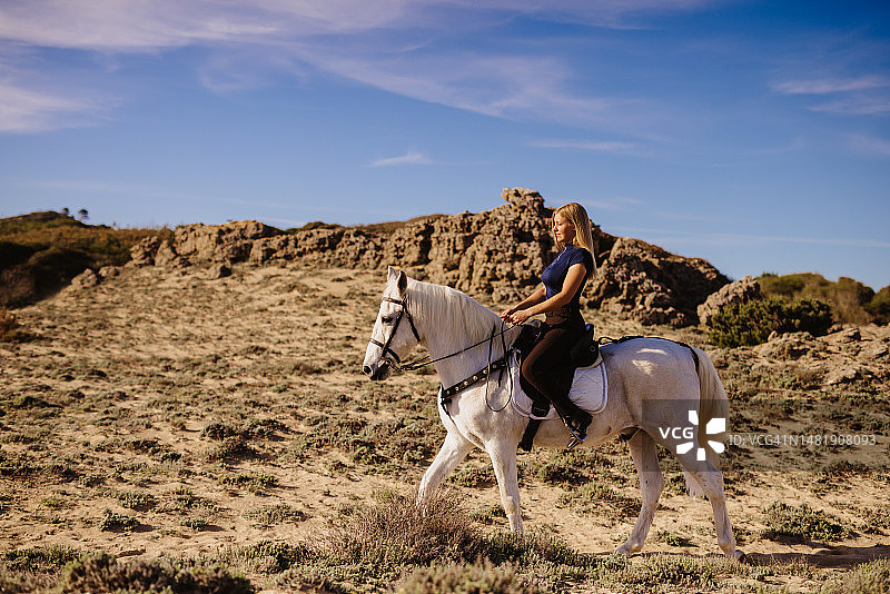 骑着白马在沙丘中穿行的年轻金发女子图片素材