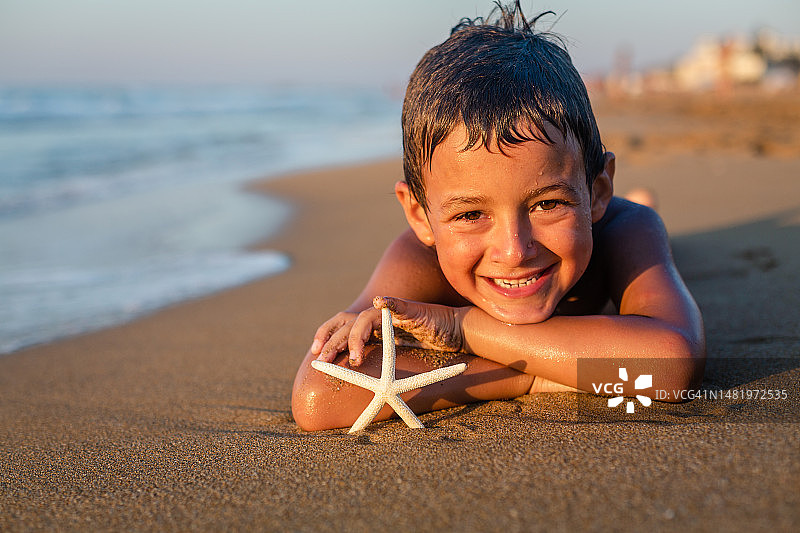 微笑的男孩在岸边看海星图片素材