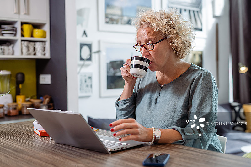 中年妇女喝着咖啡，使用笔记本电脑图片素材