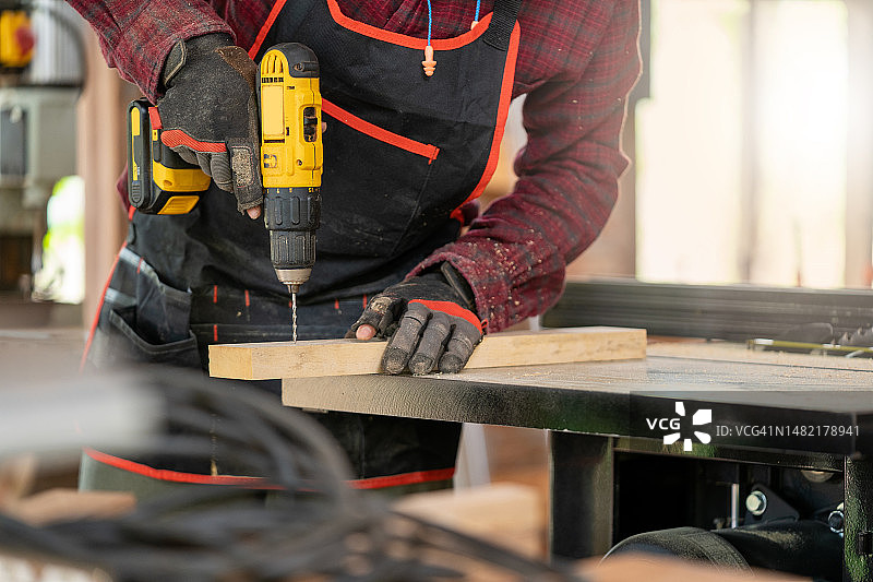 木匠在木工车间的长凳上用电钻在木板上钻孔，准备家具图片素材