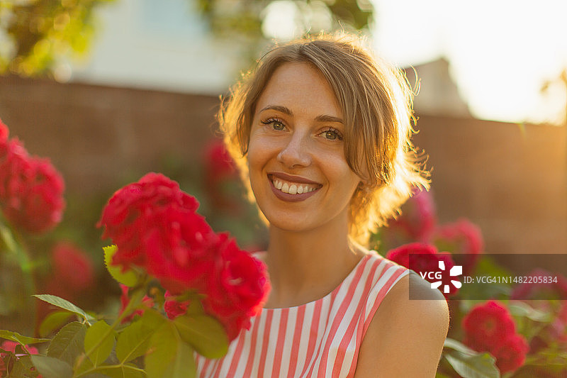 玫瑰丛背景下的连衣裙金发女人，花园春景图片素材