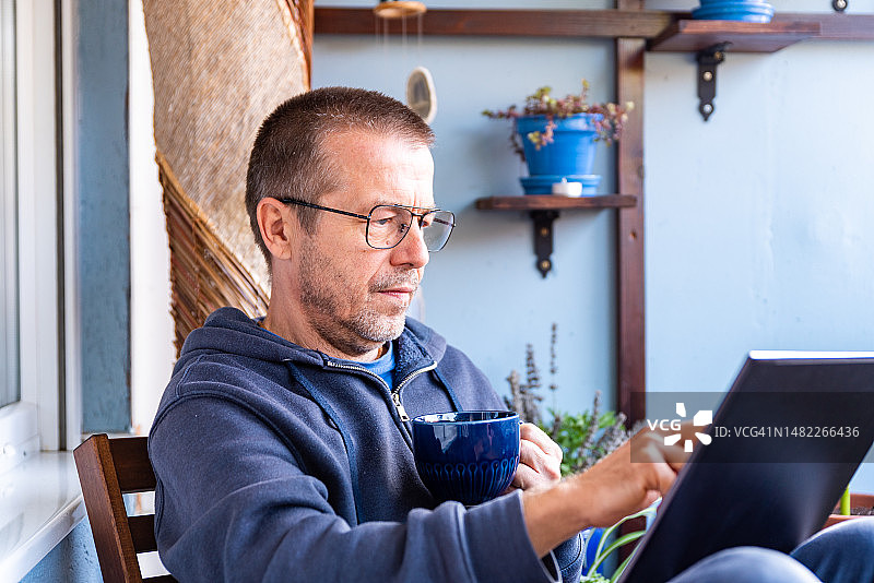 男子用笔记本电脑在家工作，在阳台上放松和喝咖啡图片素材