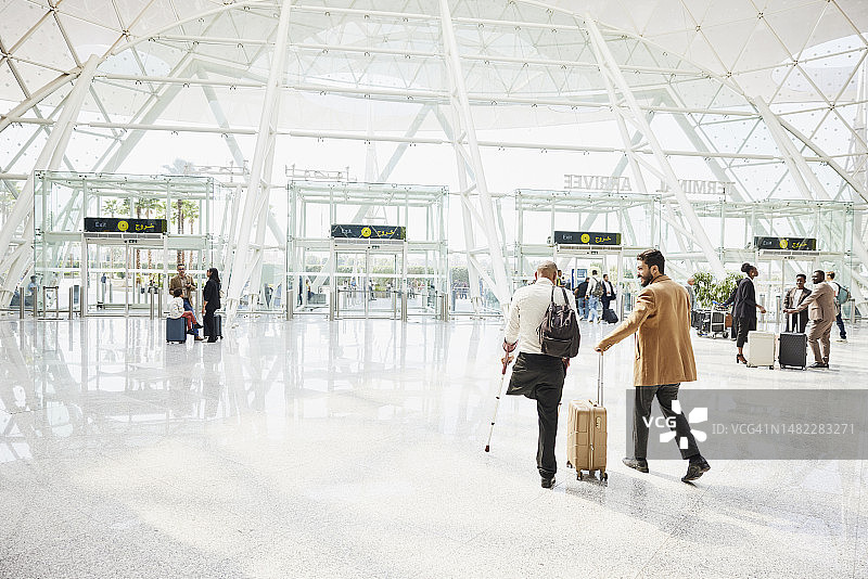 残疾男子和朋友走过机场到达区的广角镜头图片素材