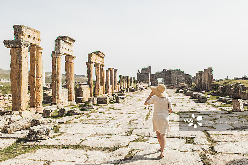 从背后看，一位女游客走过拥有被毁坏的古老柱子的古老城镇图片素材